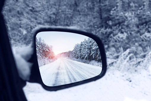 The winter road is reflected in the rear mirror of the car. Close-up.