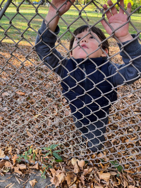 istock Little boy standing behind fence 1833227927