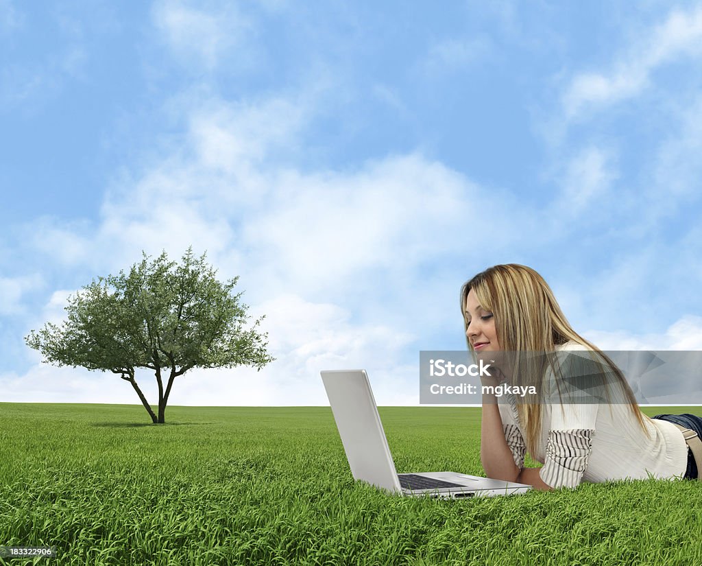 Using Computer in Nature A happy young girl lying down on grass and using computer (laptop) with cloudy sky background. 20-29 Years Stock Photo