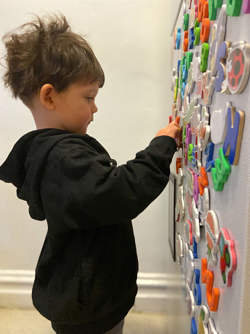 View of a little cute boy toddler playing with magnet letters on a fridge