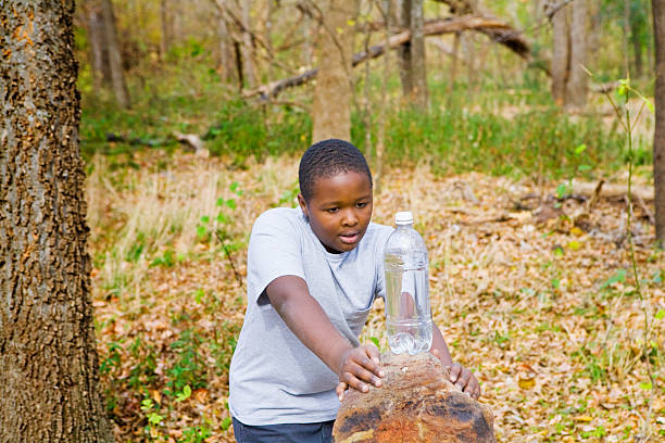 Boy in the woods looking at a bottle of water on a rock.