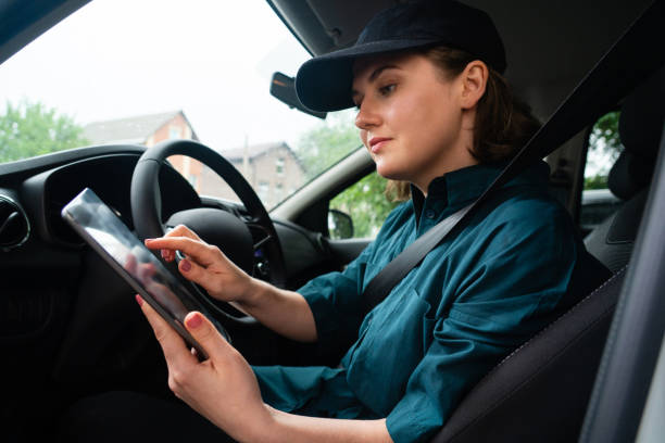 istock Woman courier sitting in a car and looking at a digital tablet. 1833244126
