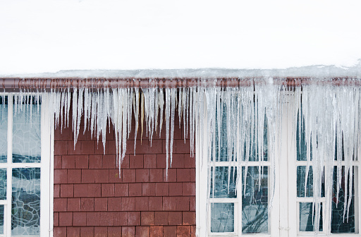 The build-up of ice and snow causing ice dam and icicles on the roof and rain gutter, causing winter damage to a house in Minnesota, USA.