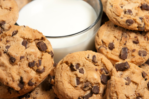 Golden brown chocolate chip cookies piled up around a glass of milk. Narrow depth of field.See related cookie images:
