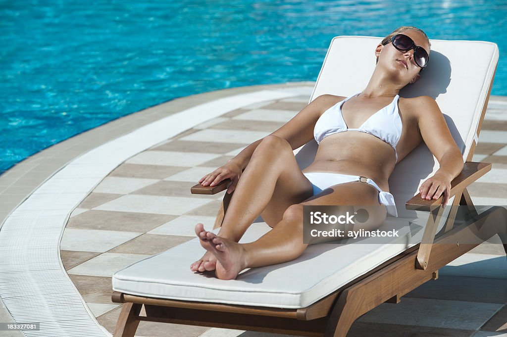 Young woman sunbathing near swimming pool. Young woman relaxing near the swimming pool at tourist resort. Adult Stock Photo