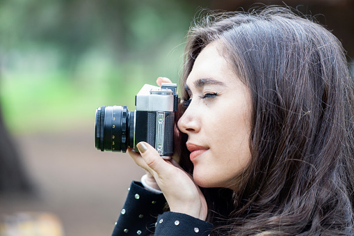 Beautiful young woman photographer taking picture outdoors with an analog camera.