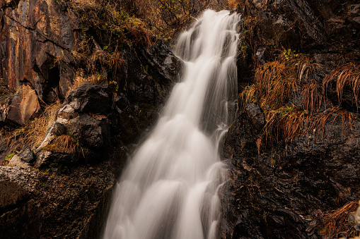 mountain stream in autumn, with the water flowing down a small waterfall and with long exposure effect. district of Paularo, F.V.G. region, Italy