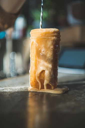 A glass jar filled with espresso tonic, the liquid is dripping off the top of the jar