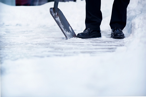 Cut view of legs and snow shovel clearing a path. Well dressed. Good copyspace.