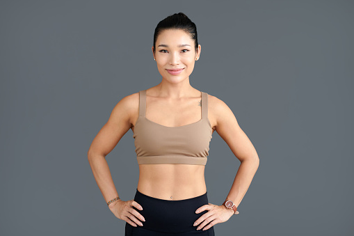 Portrait of smiling fit young woman standing against grey background