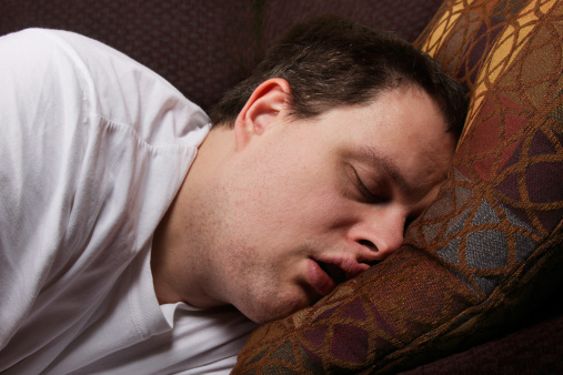A man sleeps deeply, snoring into a pillow.