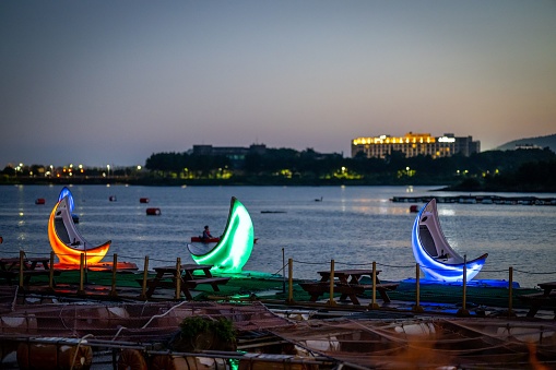 A picturesque scene of a tranquil, illuminated body of water with multiple sailboats adorned in vibrant hues of lights