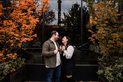 A authentic happy young multiracial couple having a coffee date in Downtown Portland Oregon. The season is autumn with colorful leafs around the city streets and buildings.