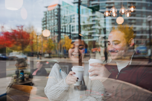 A authentic happy young multiracial couple having a coffee date in Downtown Portland Oregon. The season is autumn with colorful leafs around the city streets and buildings.