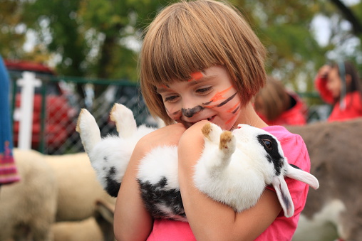 little girl with painted tiger face holds rabbit