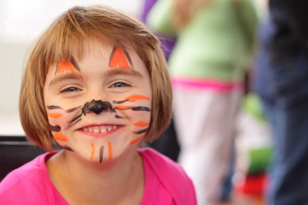 Little girl with face painted like tiger smiles at camera stock photo