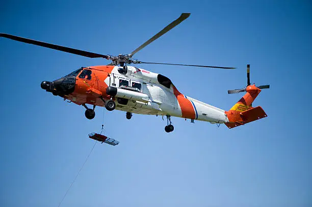 Coast Guard HH-60J Jay hawk  lowering rescue litter with a clear blue sky background.