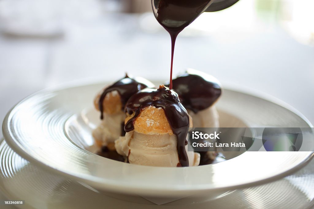 Closeup picture of profiteroles bathing in chocolate profiteroles filled with ice cream being drizzled with chocolate sauce Dessert - Sweet Food Stock Photo