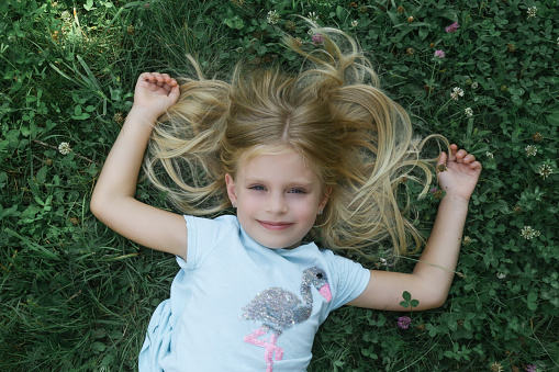 Adorable little girl with long blonde hair laying in the meadow