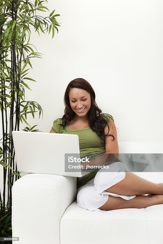 Giovane donna sul divano con il computer portatile - Foto stock royalty-free di Abbigliamento casual