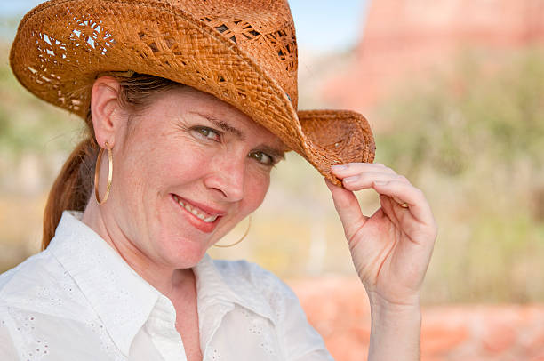A beautiful woman in her 40s wearing a cowboy hat. Natural lighting and no retouching on her flawless complexion.