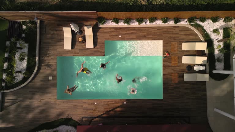 A group of young people and children jump into the pool during a summer day in the backyard.