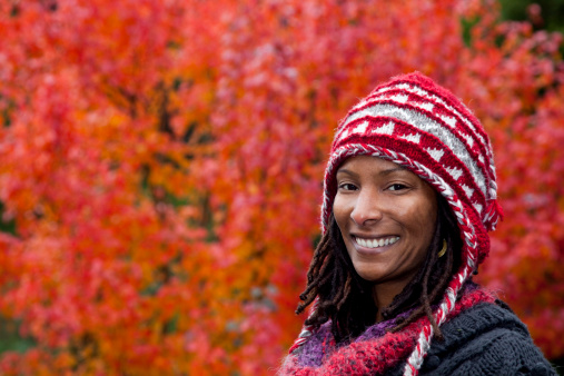 smiling Black woman wearing wool hat in front of red Maple leaf tree - copy space