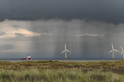 Brave the elements with this captivating image of a sturdy ship navigating through a storm, passing by a majestic offshore windfarm. The turbulent seas and dramatic sky set the stage for a powerful scene, capturing the resilience of the vessel against the backdrop of towering wind turbines. A testament to the intersection of nature's fury and human ingenuity