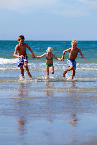 three children running in the water along the coast