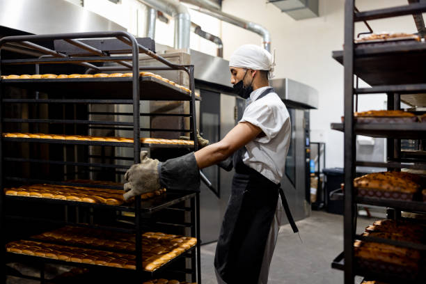 istock Man working at an industrial bakery moving a rack of bread trays 1833455742