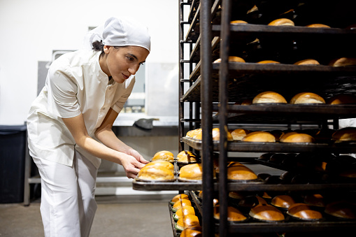 Latin American female baker baking fresh bread at an industrial bakery - food processing plant concepts