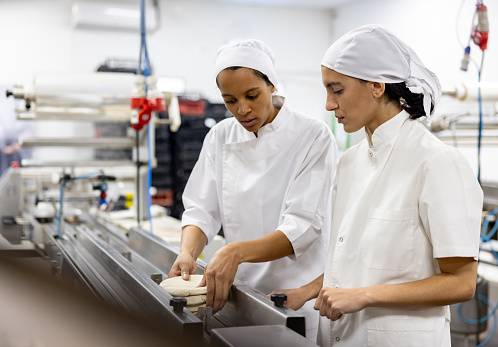 Latin American supervisor training a new worker at an industrial bakery - food processing plant