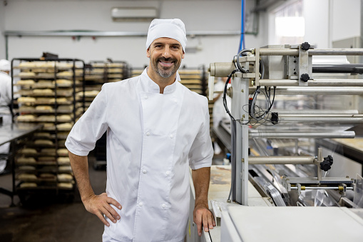 Portrait of a happy Latin American baker working at an industrial bakery and looking at the camera smiling