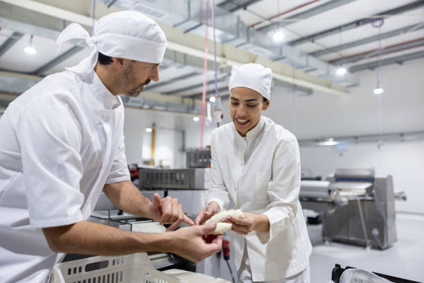 istock Man training a new worker at an industrial bakery 1833457423