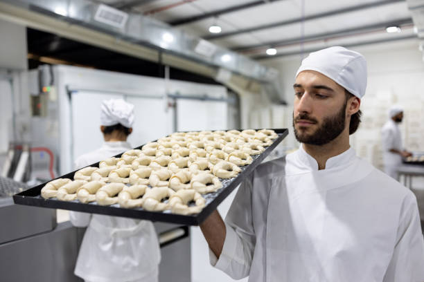 istock Baker carrying a tray of raw croissants at a bakery 1833457431