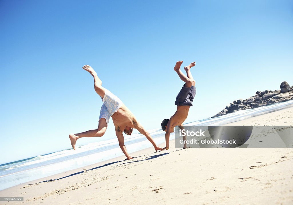 Padre e figlio facendo cartwheels sulla spiaggia - Foto stock royalty-free di Famiglia