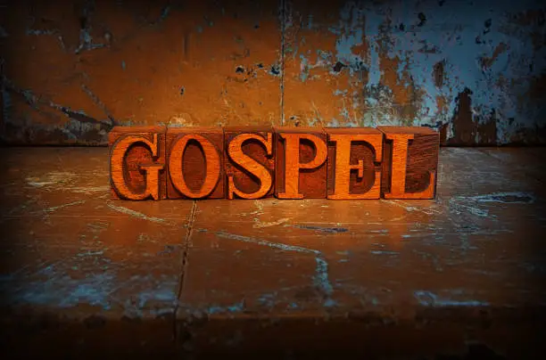 "Gospel spelled out in letterpress letters on a grunge background, lit with a torch"