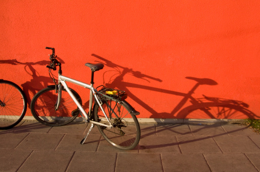 Two bicycles and elongated shadows against a bright red wall. Color not enhanced. Space for copy.