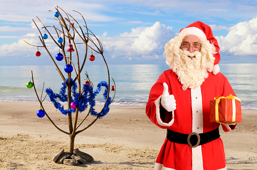 Christmas Tree and Santa Claus on a tropical beach in a sunny day.