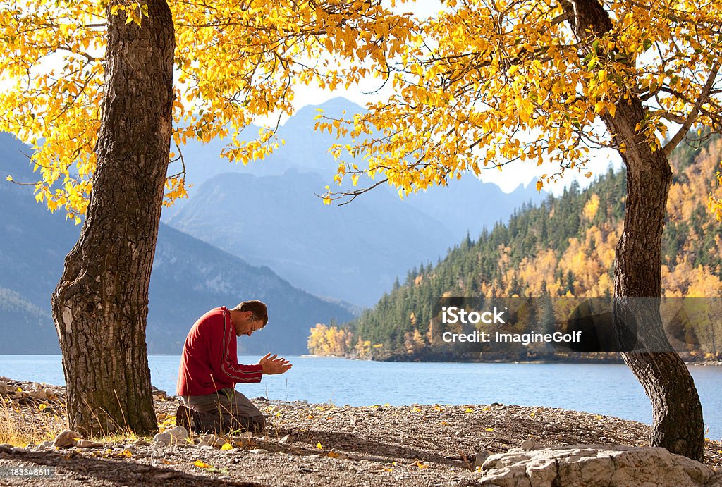 Lakeside Meditation A man prays and meditates beside a beautiful mountain lake in fall. Caucasian adult male. Side view. Praying Stock Photo
