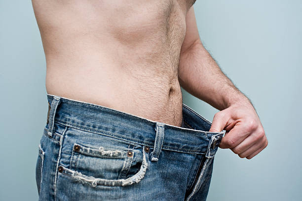 hombre mostrando pérdida de peso mostrando sus pantalones suelto - hombre flaco fotografías e imágenes de stock