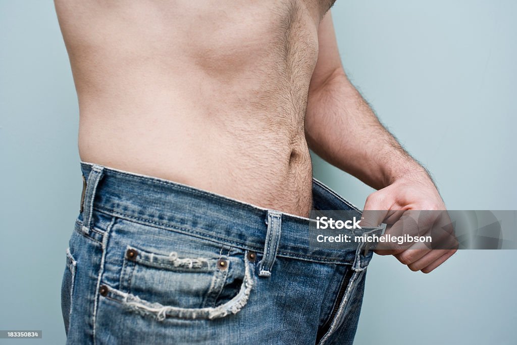 Man showing weight loss by showing his loose pants Man stands with a pair of oversize blue jeans focussing on his weight loss Men Stock Photo