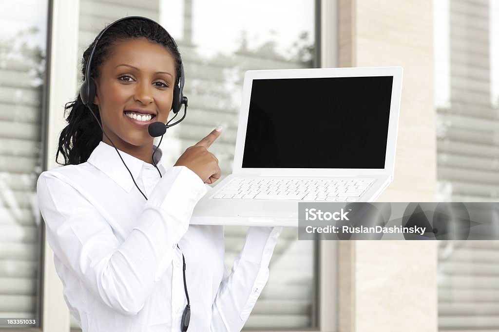 Operator pointing at computer display. Young woman operator holding up white laptop in one hand and pointing with another hand at laptop's display. Similar images preview: Women Stock Photo