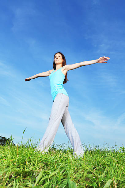 smiling mature woman in white standing in yoga pose in meadow