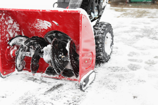 A snowblower has just finished clearing the driveway during a winter snow storm as falling snow continues to swirl.