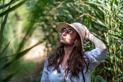 a young woman with sunglasses stands among the reeds and looks towards the sun