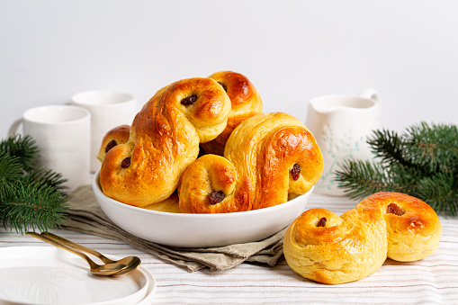 Homemade  swedish St Lucia saffron buns. on a white table. Also called  lussekatt or lussebulle, Cornish tea treat bun or revel bun, is a spiced yeast-leavened sweet bun flavoured with saffron and contains dried  raisins. Christmas decoration.