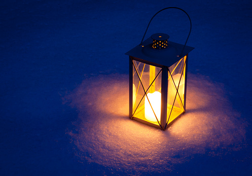 Candle lantern in snow photographed at dusk with long exposure. Copy space to the left.