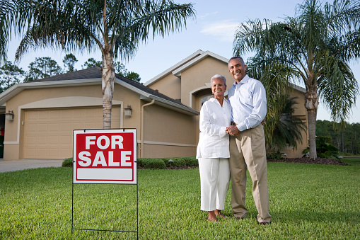 Happy African American couple outside house with for sale sign in front yard