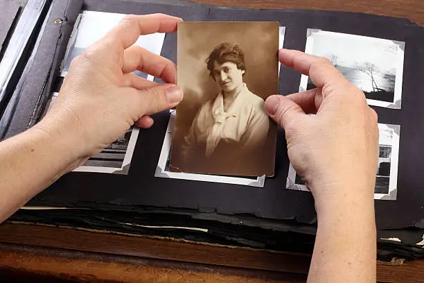 Photo of Hands holding a sepia photograph above a phot album